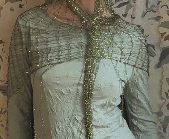 Close-up of the mesh worn as a shoulder cape over sage silk, knotted like a spider's web.