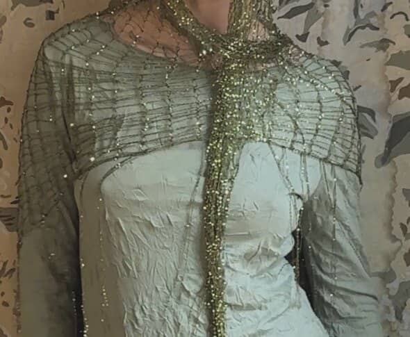 Close-up of the mesh worn as a shoulder cape over sage silk, knotted like a spider's web.